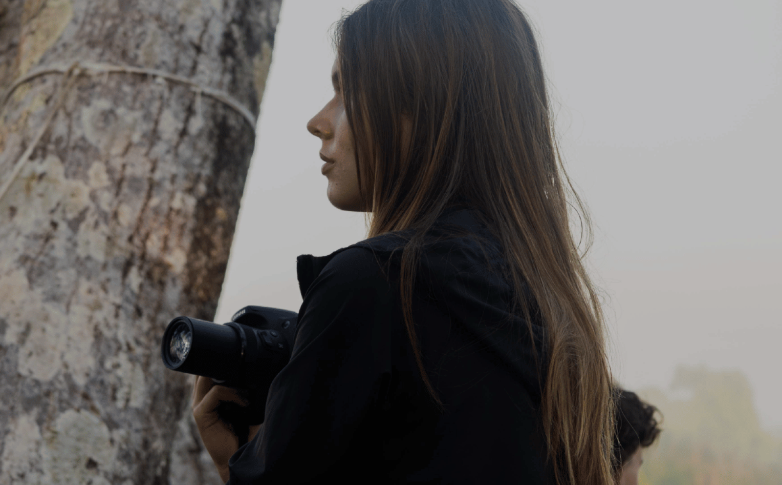 A female volunteer holding a camera looks out over the canopy in the Amazon rainforest, Peru